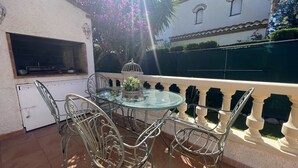 An outdoor patio with a glass table and metal chairs, a grill, and a decorative birdcage with flowers. - MASIA4 adosado con piscina comunitaria (Miami Playa)