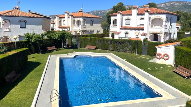 A swimming pool with a clear blue water, surrounded by well-maintained grass and hedges. - MASIA4 adosado con piscina comunitaria (Miami Playa)
