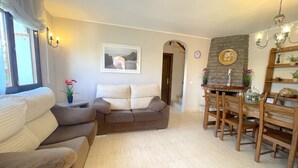 A living room with a sofa, a dining table with chairs, a fireplace, and a clock on the wall. - MASIA4 adosado con piscina comunitaria (Miami Playa)