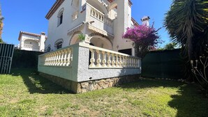A white building with a balcony, a stone wall, and a green fence. - MASIA4 adosado con piscina comunitaria (Miami Playa)