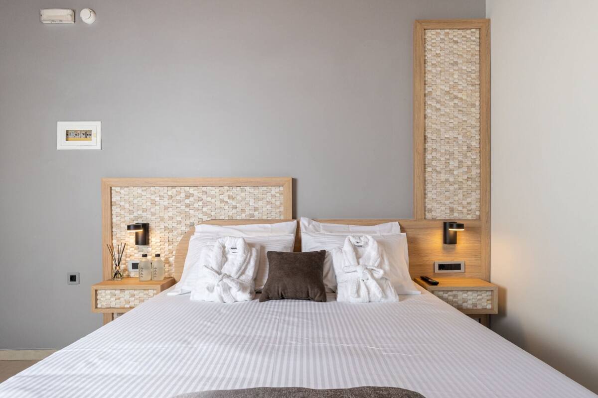 Un lit bien fait, avec du linge de lit blanc, une tête de lit ornée d’un motif en mosaïque et deux tables de chevet avec des lampes.