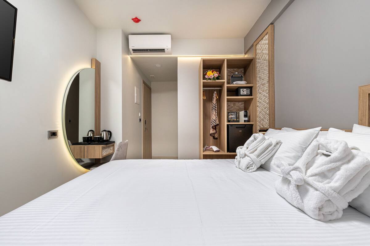 Une chambre d’hôtel moderne dotée d’un grand lit, d’une coiffeuse avec miroir, d’une armoire et d’un petit coin salon.