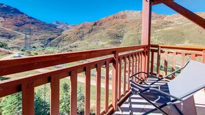 Un balcón con vistas a montañas, una silla y una mesa.