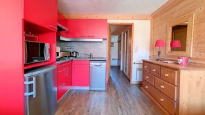 Cocina compacta con armarios rojos, electrodomésticos de acero inoxidable y un mueble de madera con espejo y lámpara.