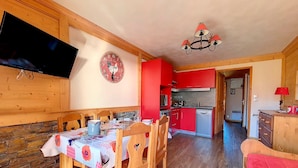 Un comedor con muebles de madera, un televisor montado en la pared y una cocina al fondo.