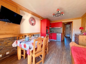 Zona pranzo con arredi in legno, una televisione a parete e una cucina sullo sfondo.
