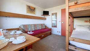 A cozy room with a wooden bench, a sofa, a bunk bed, and a dining table set with white dishes and glasses. - Cozy studio at the foot of the slopes with balcony (Les Menuires)