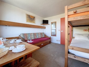 A cozy room with a wooden bench, a sofa, a bunk bed, and a dining table set with white dishes and glasses.
