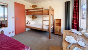 A bunk bed room with a wooden table set for dining, a window with curtains, and a door. - Cozy studio at the foot of the slopes with balcony (Les Menuires)
