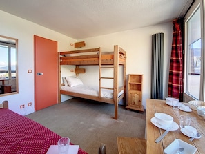 A bunk bed room with a wooden table set for dining, a window with curtains, and a door.