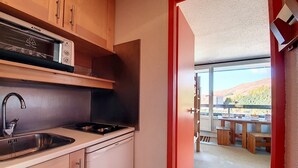 A compact kitchen with a sink, stove, and cabinets, leading to a dining area with a table and chairs. - Cozy studio at the foot of the slopes with balcony (Les Menuires)