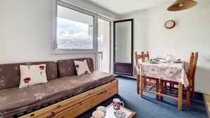Un'accogliente stanza con un divano, un tavolo da pranzo con sedie e una finestra vista montagne innevate.