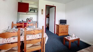 Una stanza compatta con un letto, un piccolo tavolo di legno, una televisione e un angolo cottura.