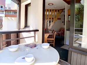 Un comedor con una mesa redonda preparada para cuatro personas, una escalera de madera y vistas al balcón exterior.