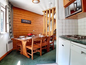 A compact kitchen with wooden walls, a dining table with chairs, and a microwave above the counter. - Charming duplex 6 pers, near slopes, north balcony, WiFi (Les Menuires)