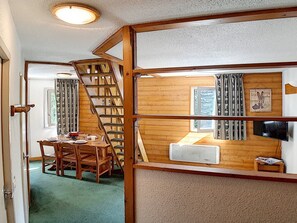 A room with a wooden staircase, a dining area with a table and chairs, and a television on a wooden shelf. - Charming duplex 6 pers, near slopes, north balcony, WiFi (Les Menuires)