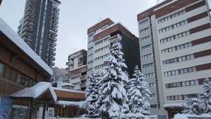 Ein verschneiter Innenhof mit einem Mehrstöckiger Gebäude und Balkonen, umgeben von mit Schnee beladenen Bäumen.