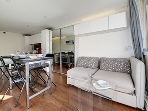 Un salon moderne comprenant un canapé, une table à manger, des chaises et un coin cuisine visible à travers une cloison en verre.
