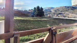 Blick aus einem Gebäude auf eine Rasenfläche mit Holzzaun, ein entferntes Gebäude und ein Gebirge.