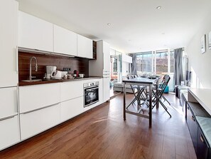 Une cuisine moderne avec des meubles blancs, un plan de travail en bois et un coin repas comprenant une table et des chaises.