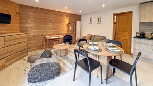 Een moderne woonkamer met een houten wand, een eettafel voor vier personen en een keukenhoek met een broodrooster.