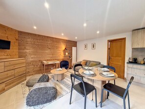 A modern living room with a wooden wall, a dining table set for four, and a kitchen area with a toaster.