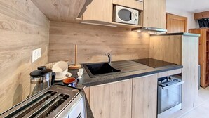 Een moderne keuken met houten keukenkastjes, een ingebouwde magnetron, een roestvrijstalen spoelbak en een compacte vaatwasser.