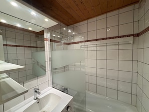 Ein Badezimmer mit Duschkabine aus Glas, einem weißen Waschbecken und einem Spiegel.