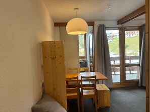 Ein Zimmer mit einem Holztisch, Stühlen, einer Bank, einer Hängelampe und Blick durch eine Glastür.