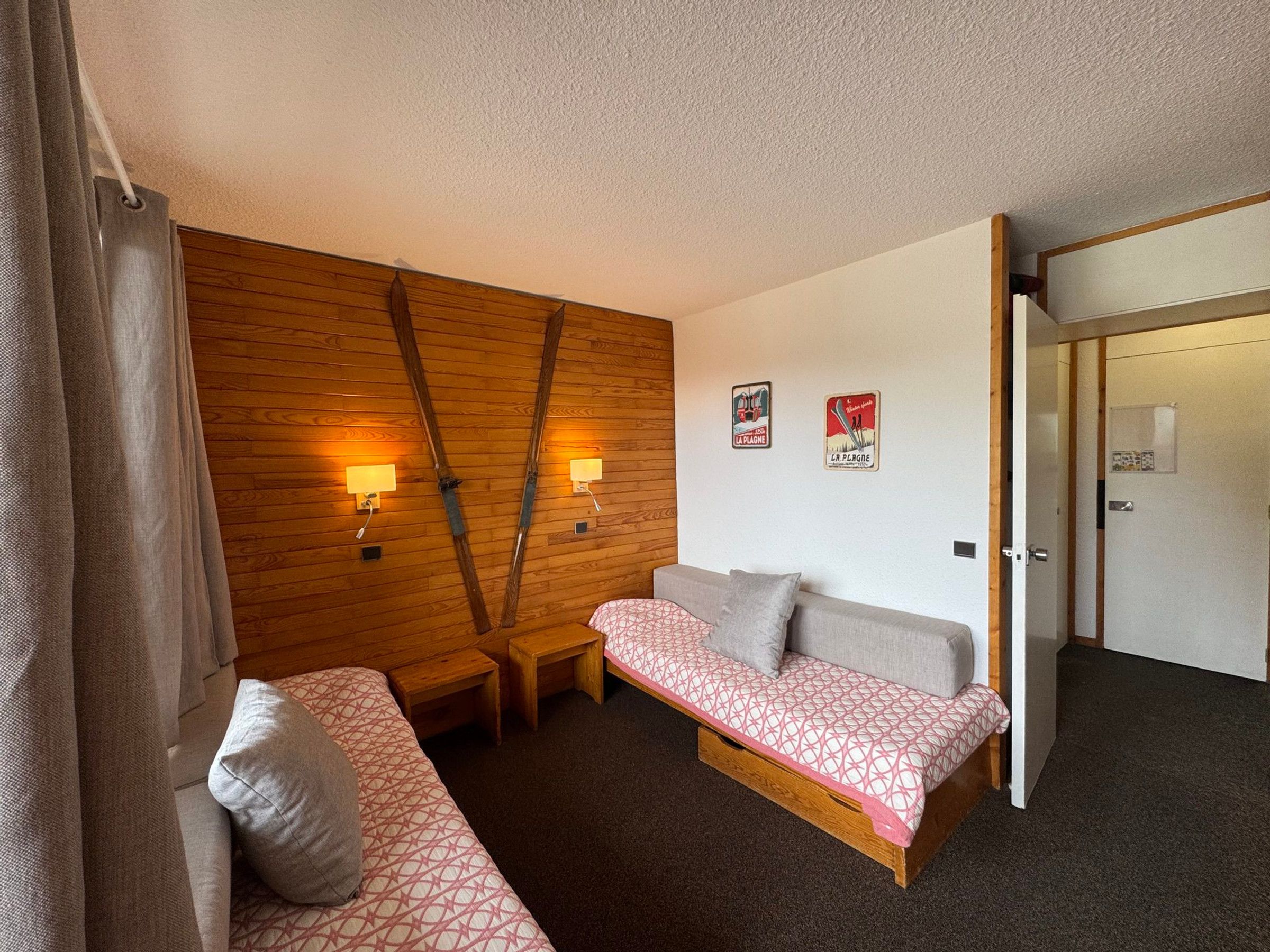 A room with a wooden wall, two bedside tables, a sofa, and a door leading to another room.