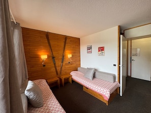 Quarto com parede de madeira, duas mesas de cabeceira, um sofá e uma porta que dá para outro cômodo.