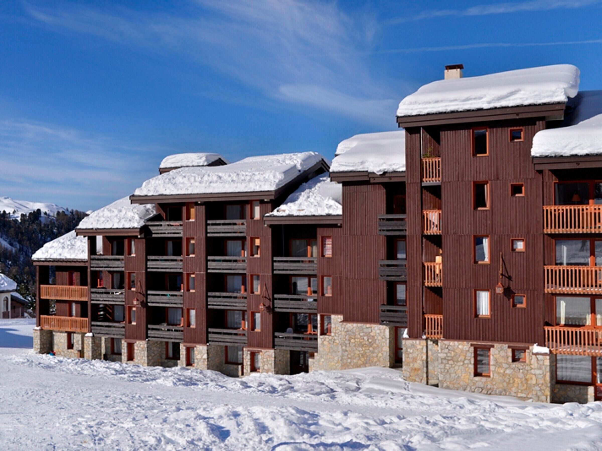 Un hotel de varios pisos con balcones y una base de piedra, rodeado de nieve.