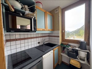 A compact kitchen with a microwave, sink, and a window with a view of the outdoors.