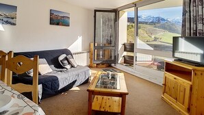 Una camera accogliente con un letto, un tavolo in legno, una TV e un'ampia finestra vista montagna.