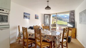 Un'area pranzo con un tavolo apparecchiato per quattro persone, sedie di legno, una ventola a soffitto e una finestra con vista sulle montagne.