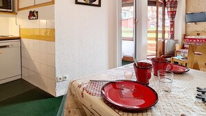 Ein gemütliches Zimmer mit einem Bett, einem Tisch gedeckt mit roten Tellern und Gläsern, einem Holz-Kopfteil und einem Fenster mit Blick ins Freie.