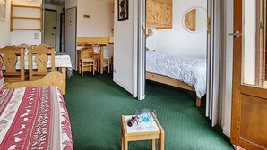 Ein kleines Zimmer mit einem Bett, einem Tisch mit Gläsern, einem Holzstuhl, einem Schreibtisch und einem Kleiderschrank.