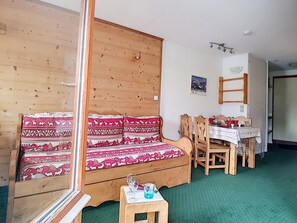 A cozy room with a wooden sofa, a dining table with chairs, and a small wooden side table with a glass.