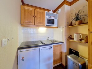 Una cocina compacta con armarios de madera, un microondas, un lavavajillas y un refrigerador pequeño.