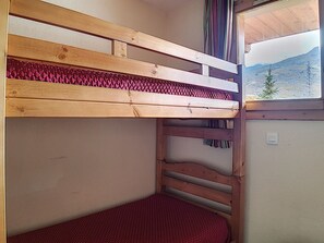 A bunk bed with a red mattress and a view of a mountain through a window.