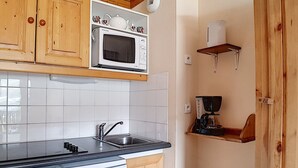 A kitchen with wooden cabinets, a white microwave, a coffee maker, and a dishwasher. - 2-room apt 4 pers, ski-in/ski-out, south balcony (Les Menuires)