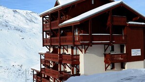 A wooden chalet with multiple balconies and a snow-covered roof, surrounded by a snowy mountain landscape. - 2-room apt 4 pers, ski-in/ski-out, south balcony (Les Menuires)