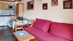A cozy living area with a red sofa, wooden dining table, and a kitchen in the background. - 2-room apt 4 pers, ski-in/ski-out, south balcony (Les Menuires)