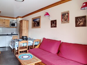 A cozy living area with a red sofa, wooden dining table, and a kitchen in the background.