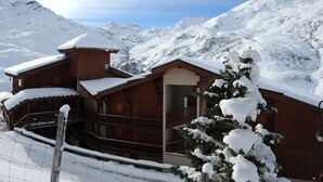 A wooden lodge with a balcony and a snow-covered mountain backdrop. - 2-room apt 4 pers, ski-in/ski-out, south balcony (Les Menuires)
