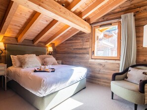 A cozy bedroom with a large bed, a nightstand, a chair, and a window with curtains. - Luxurious chalet, direct slope access, parking and WIFI included (Saint-Martin-de-Belleville)