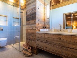 A modern bathroom with a wooden wall, a glass shower enclosure, and a wooden vanity with drawers. - Luxurious chalet, direct slope access, parking and WIFI included (Saint-Martin-de-Belleville)
