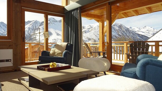 Quarto aconchegante com vista para montanhas nevadas, móveis de madeira e varanda com corrimão.