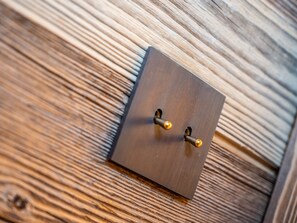 A square metallic switch plate with two gold-colored handles on a wooden surface. - Luxurious chalet, direct slope access, parking and WIFI included (Saint-Martin-de-Belleville)