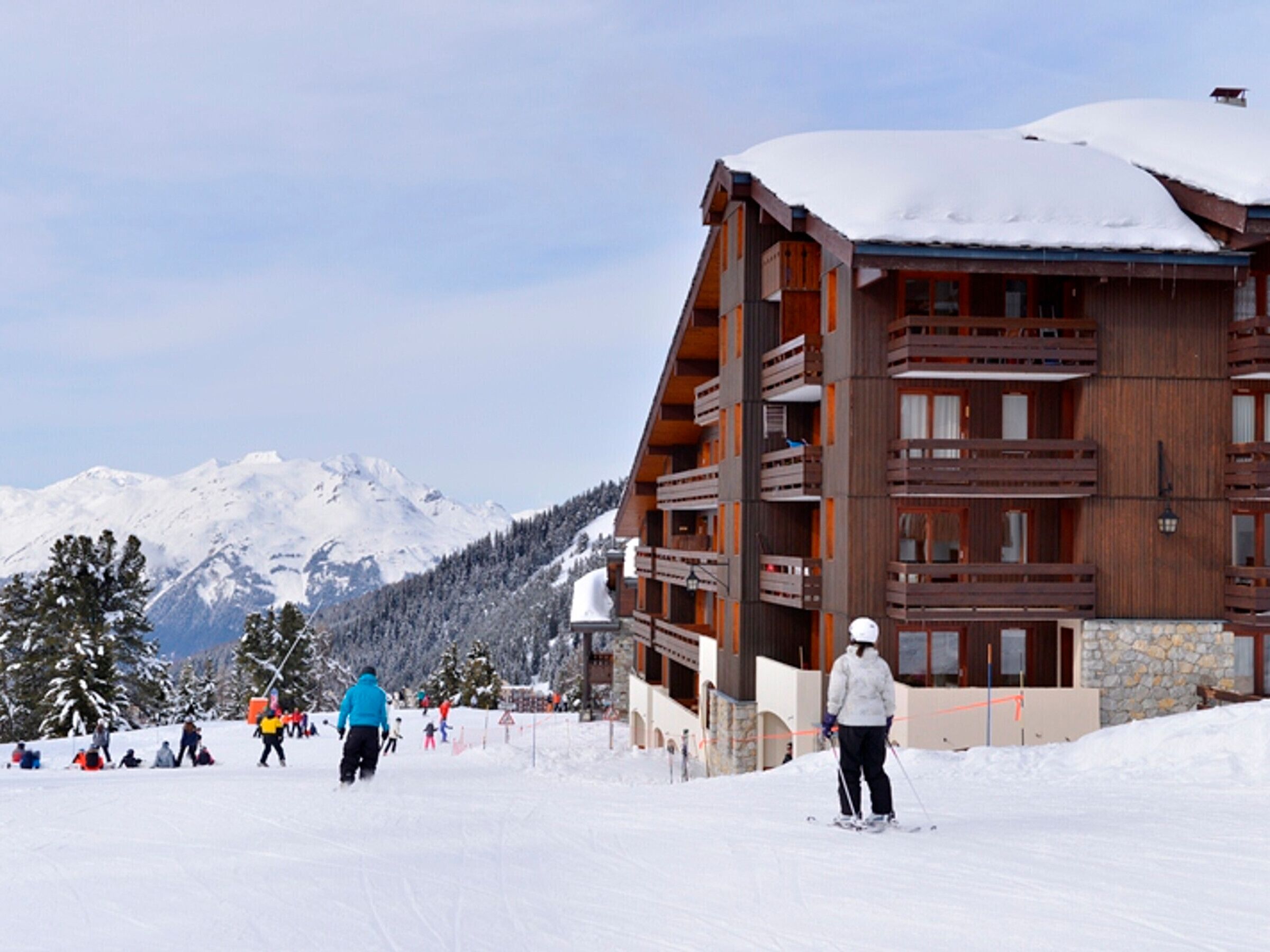A ski resort building with multiple balconies and a stone facade, surrounded by snow-covered mountains.